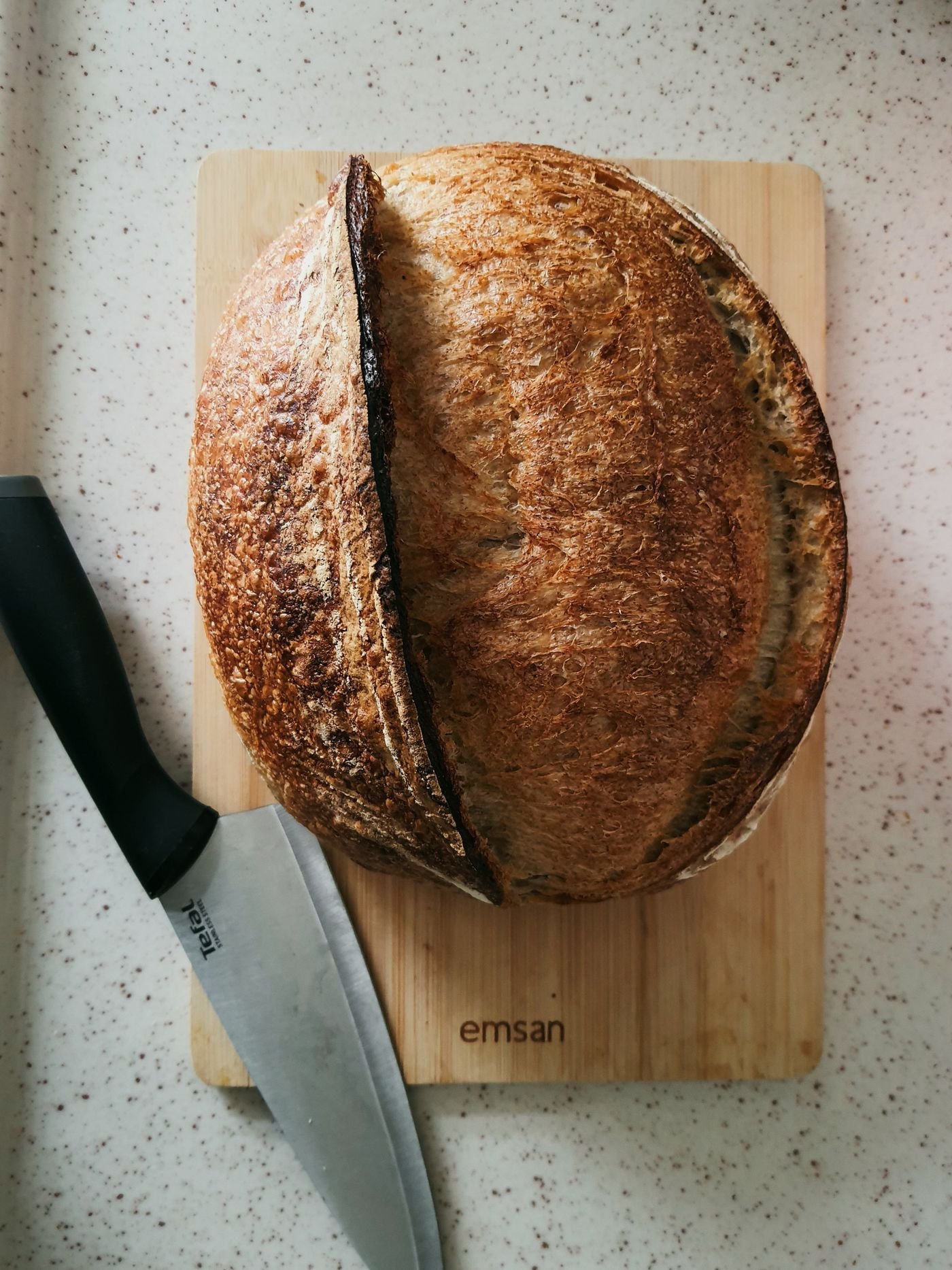 A round sourdough loaf on a board with a bread knife